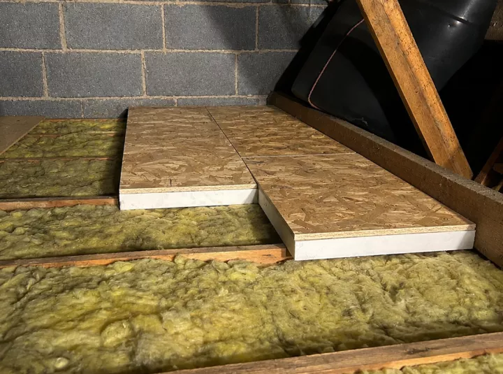 Attic insulation with wooden planks, sloped beams above.